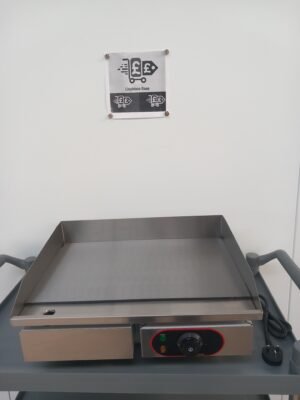 Front view of a 55cm commercial griddle with a flat stainless steel cooking plate, partially visible temperature controls, and an easy-access oil waste collection drawer for efficient commercial kitchen use.