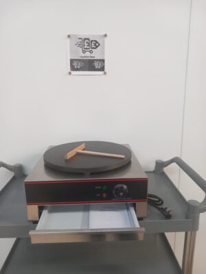 Front view of a commercial 400mm crepe maker with Teflon-coated plate, crepe spreader on the cooking surface, and drawer below open to display the user manual, designed for easy operation in commercial kitchens.